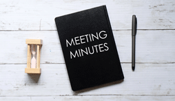 A notebook for meeting minutes, lies between a pen and an hourglass