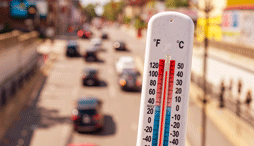 A thermometer showing a temperature of 100+ against a background of an urban street