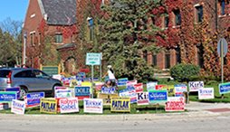 A bicyclist rides pass a variety of election related yard signs