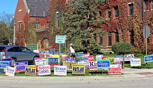 A bicyclist rides pass a variety of election related yard signs