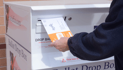 A person putting a ballot into a ballot box