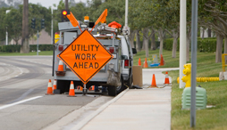 Utility trucked parked on sidewalk with a road sign noting that utility work is being done