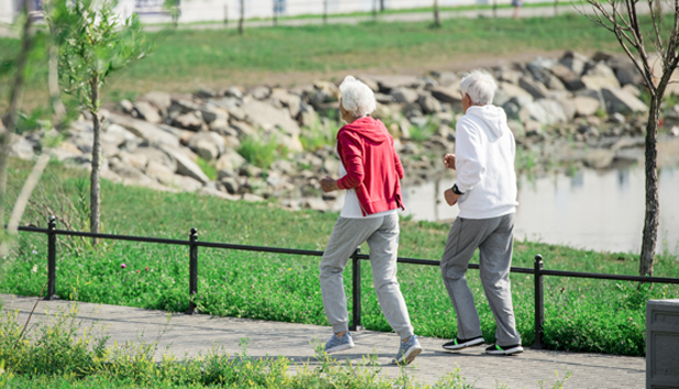 Active senior couple running outdoors in park along lake