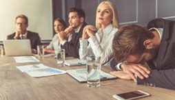 During a meeting of a small group around a table, one of the members puts his head down on the table because he is dismayed at what is happening.