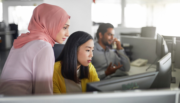 Female colleagues, one wearing a hijab, working at computer desk