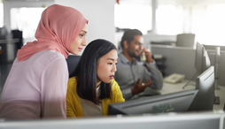 Female colleagues, one wearing a hijab, working at computer desk