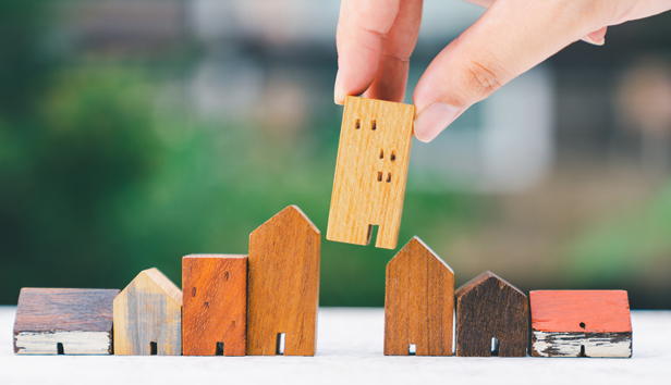 Close up of a hand choosing a mini wooden house from among several models offered