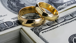 Two gold wedding rings on a stack of US $100 dollar bills