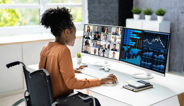 A woman in a wheelchair attends a remote work meeting from home using a desktop computer.