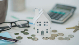 A close up of a model of a building against scattered coins, keys, and a calculator,  representing a landlord renting property