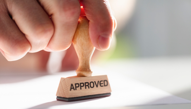 A hand holds a stamp labeled "approved"