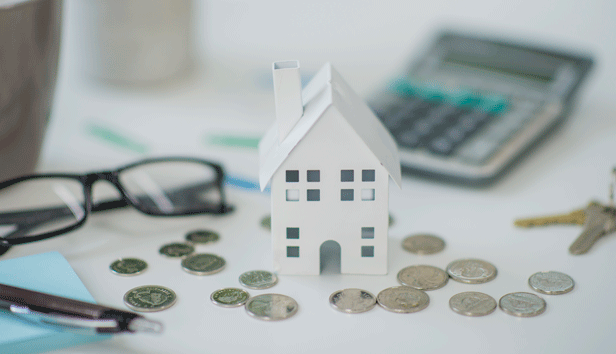 A close up of a model of a building against scattered coins, keys, and a calculator,  representing a landlord renting property